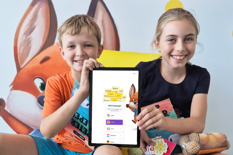 Kids smiling and holding up a tablet with KOBI - Happy Reading app open.